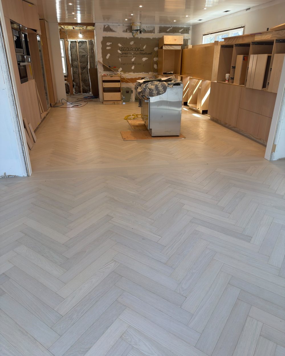 Light grey herringbone wood floor in a kitchen under renovation